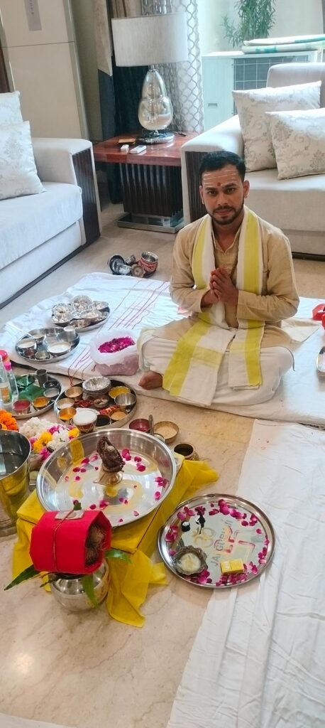 Vandanam pandit with folded hands beside the full puja setup at a home in Delhi