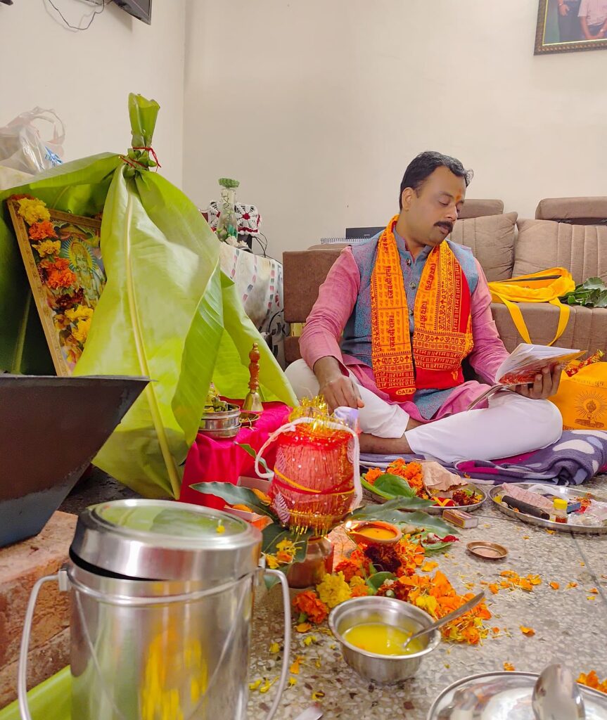 Vandanam pandit reciting the katha from the gutka at a family home, with kalash and marigold