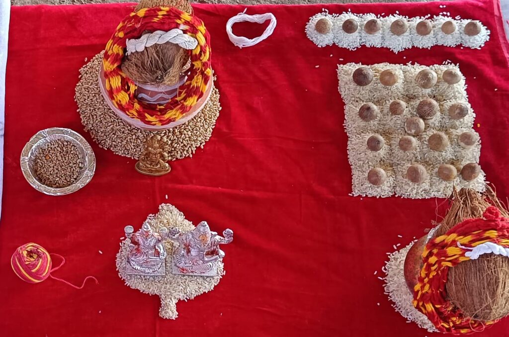 Puja samagri laid out on red cloth with a decorated kalash, silver Ganesh and Lakshmi idols, rice and supari