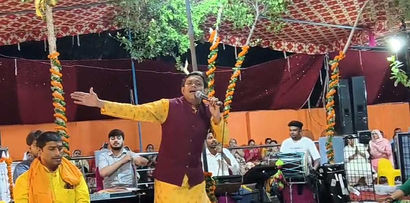 A mandali singer performing live with dholak and musicians at an outdoor decorated puja event