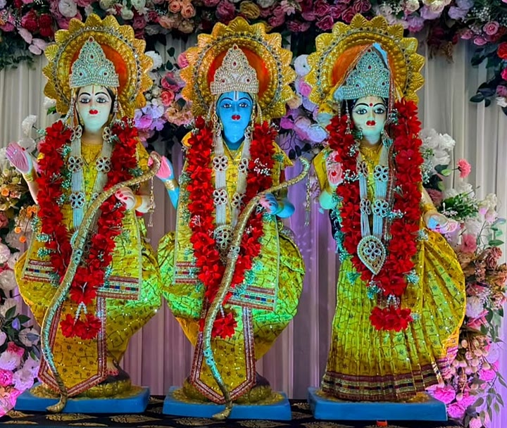 Close-up of Ram, Lakshman and Sita idols with gold crowns and red flower garlands against a white floral backdrop